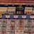 A colorful board game layout with intricate patterns and game pieces. The board features rows and columns with different symbols and tracks, including small structures resembling buildings and pawn-like figures in blue, red, and yellow.